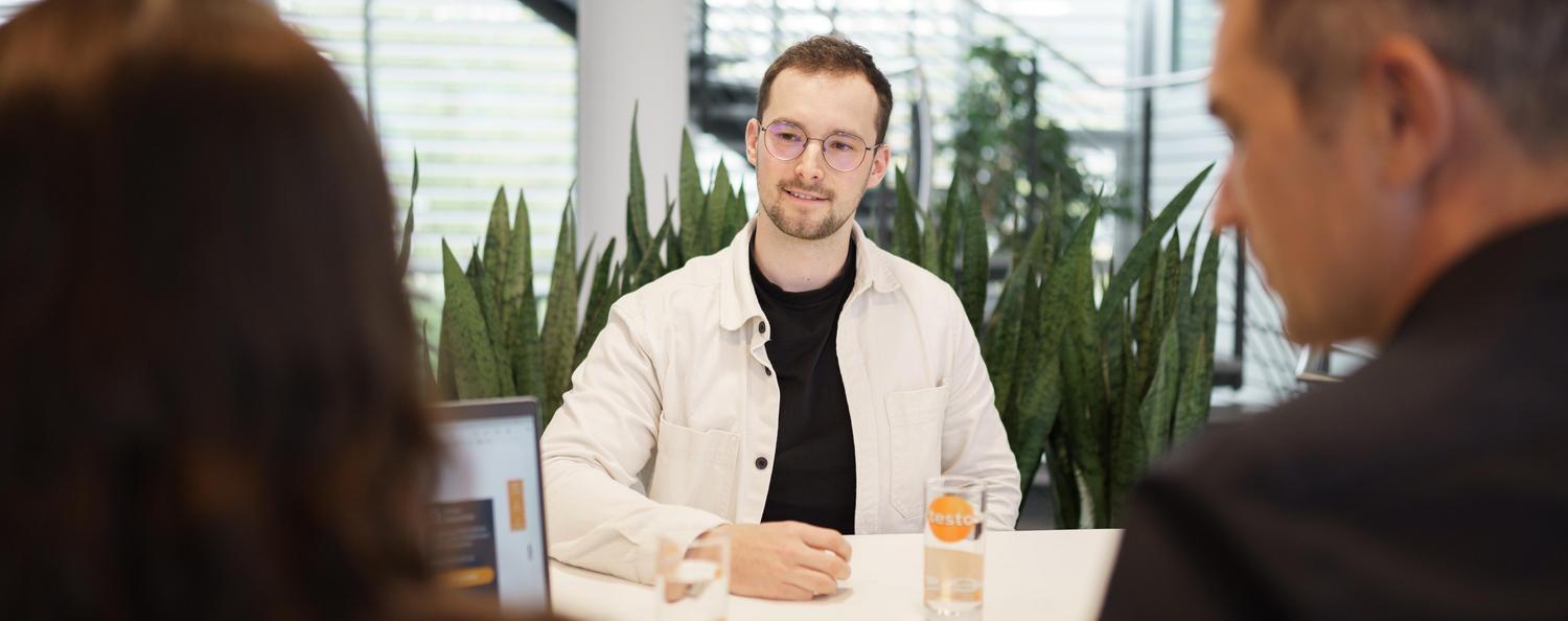 Mathias Rombach, Ausbildungsleiter lächelt in die Kamera. Eine Kollegin sitzt neben ihn und lacht.