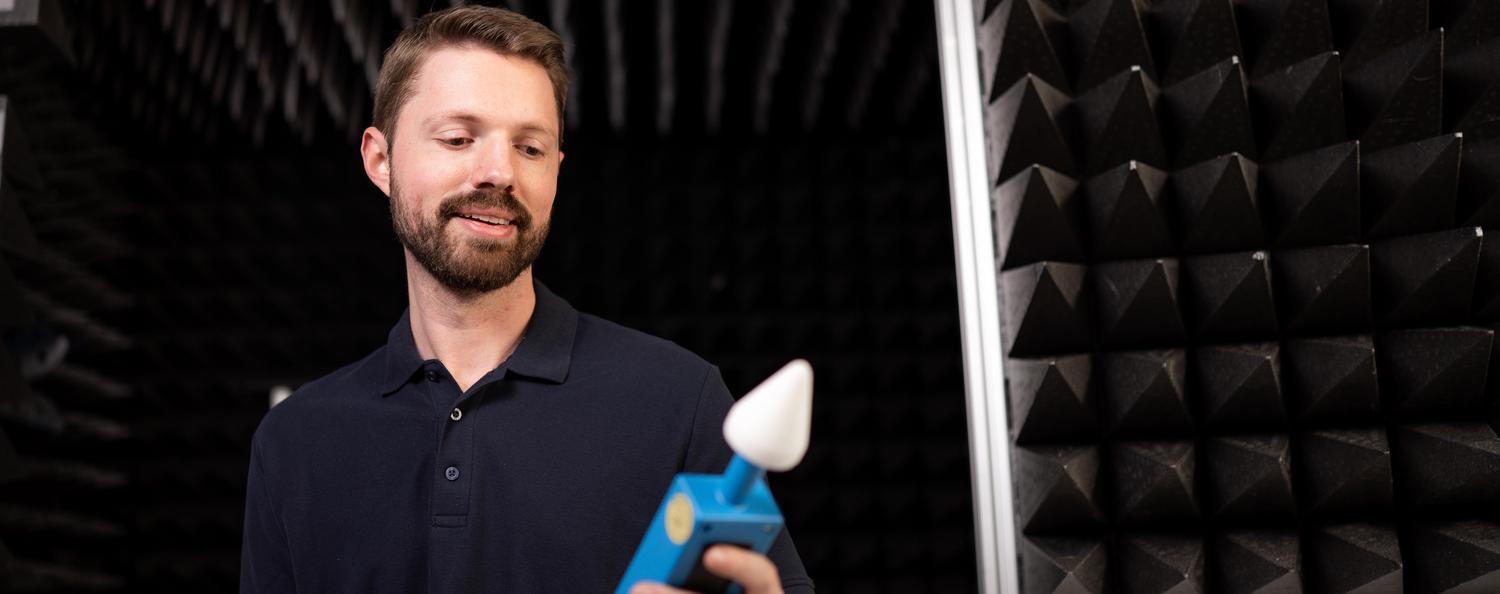 Mann schaut auf Mikrowellenlecktester. Im Hintergrund sieht man eine E-Feld-Kammer.