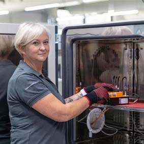 Ansicht einer Frau im Seitenprofil. Am rechten Bildrand steht ein Klimaschrank, an dem die Frau arbeitet.