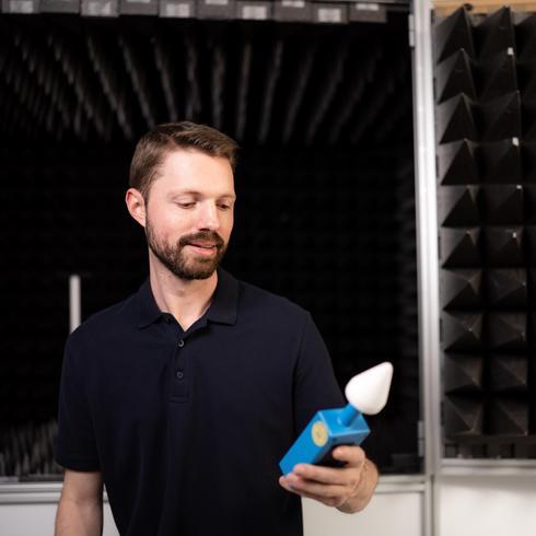 A man holds a microwave leak tester in his hand in front of the E-field calibration chamber.