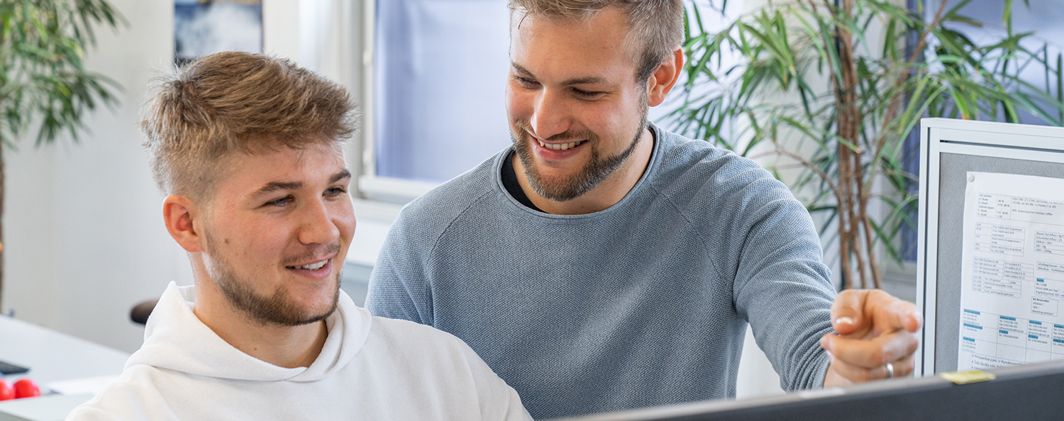 Ein angehender Fachinformatiker und sein Ausbilder arbeiten gemeinsam am Computer und beraten sich. 