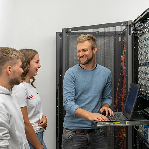 Ein IT Mitarbeiter zeigt zwei Praktikanten den Serverraum.