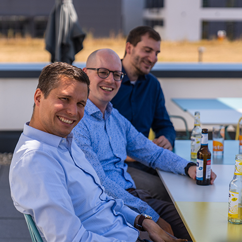 Jonas, Sebastian und Philipp sitzen hintereinander, lachen in die Kamera und trinken ein Bier