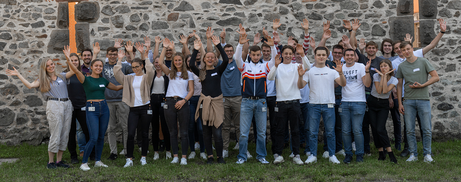 Unsere neuen Azubis 2021 Die neuen Azubis stehen vor einer Mauer und jubeln.