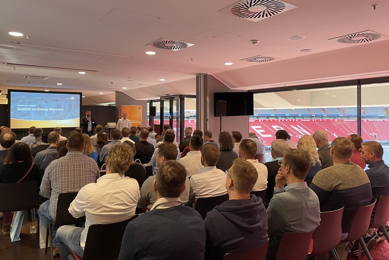 Teilnehmende hören sich einen Vortrag bei der Veranstaltung Qualität im Dialog in München an