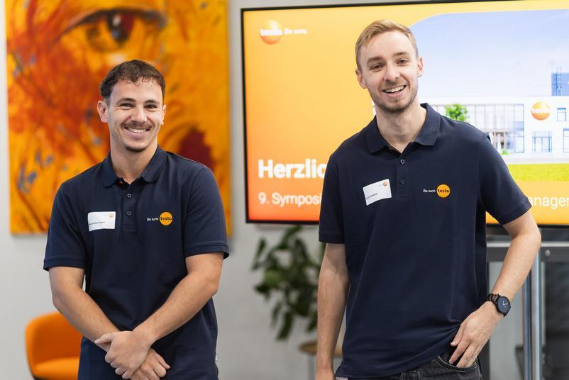Symposium Kalibrierung & Prüfmittelmanagement 2026 Zwei Mitarbeitende von Testo Industrial Services stehen vor einem Bildschirm mit der Begrüßungsfolie des Symposiums Kalibrierung und Prüfmittelmanagement.