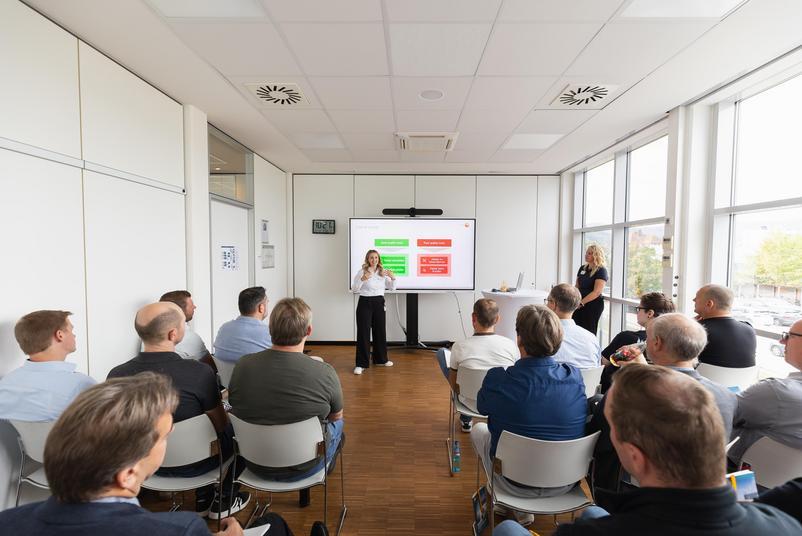 Symposium Kalibrierung & Prüfmittelmanagement 2026 Teilnehmende sitzen in einem hellen Seminarraum und verfolgen einen Fachvortrag. Vorne präsentieren zwei Personen Inhalte auf einem großen Bildschirm.
