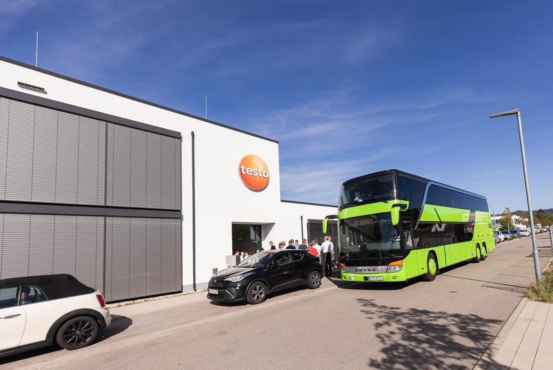 Symposium Kalibrierung & Prüfmittelmanagement 2026 Vor dem Gebäude von Testo Industrial Services steht ein grüner Reisebus. Mehrere Teilnehmende versammeln sich am Eingang des Firmengebäudes.