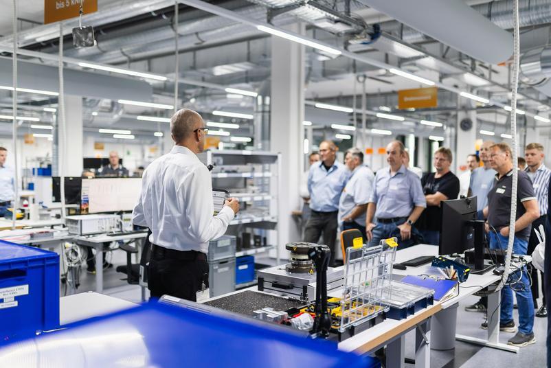 Symposium Kalibrierung & Prüfmittelmanagement 2026 Eine Gruppe von Teilnehmenden folgt einer Führung durch den Laborbereich. Eine Person erläutert die ausgestellten Arbeitsplätze und technischen Anlagen.