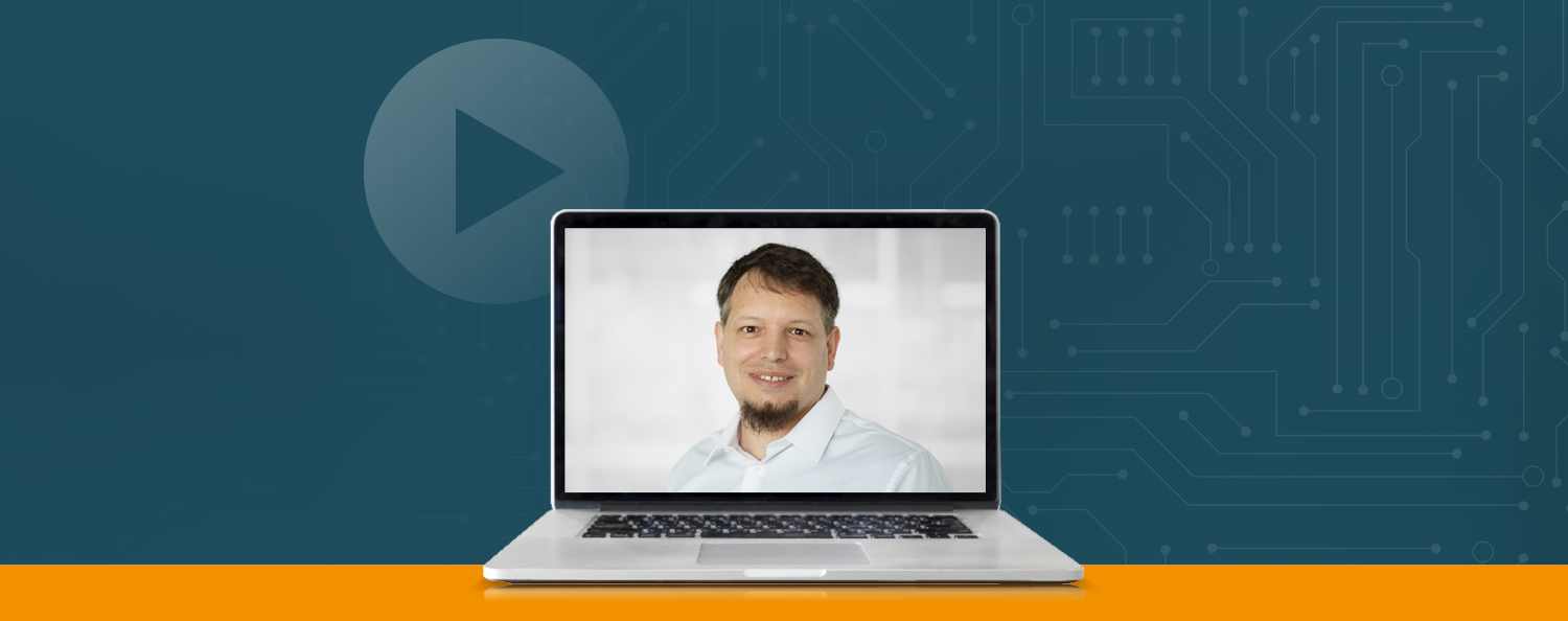 Laptop vor blauem Hintergrund. Auf dem Laptop sieht man den Referent im Portrait.
