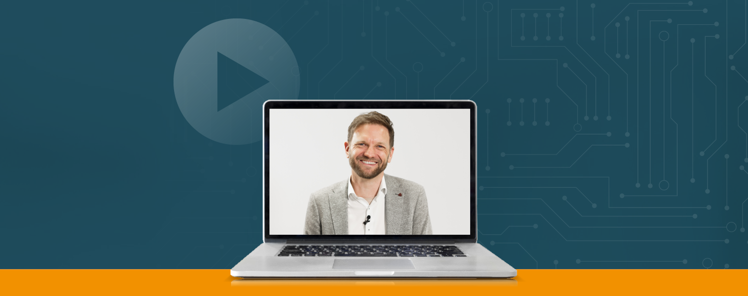 Laptop vor blauem Hintergrund. Auf dem Laptop sieht man den Referent im Portrait.