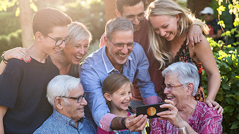 Verschiedene Generationen genießen ihre Freizeit, lachen und schauen auf ein Smartphone.