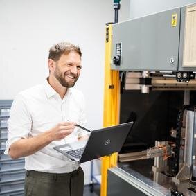 Mann mit Laptop steht vor einen Drehmomentprüfstand